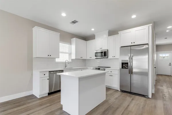 a kitchen with stainless steel appliances granite countertop a refrigerator a sink a stove and white cabinets with wooden floor