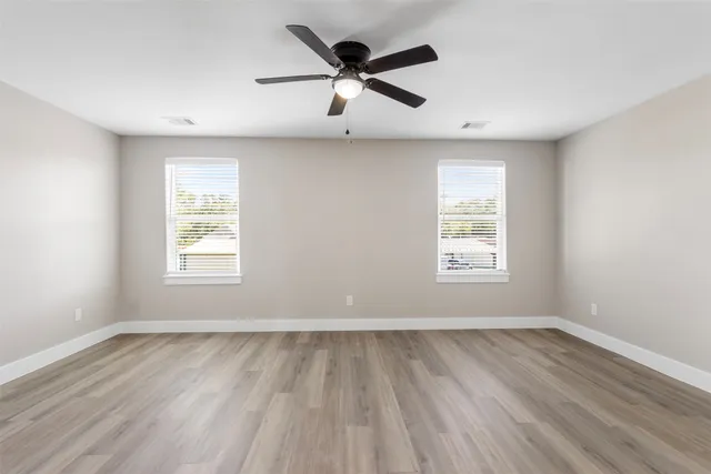 an empty room with wooden floor ceiling fan and windows