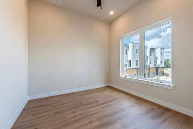 an empty room with wooden floor fan and windows