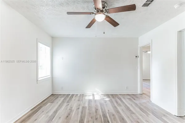 an empty room with wooden floor fan and windows