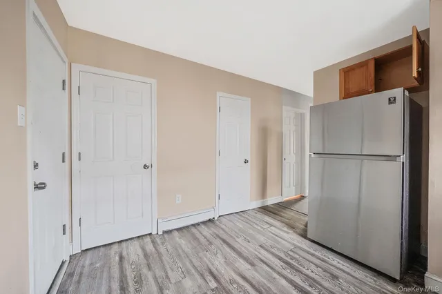 a view of an empty room with wooden floor and a refrigerator