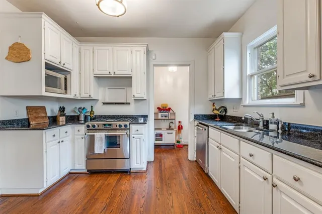 a kitchen with stainless steel appliances granite countertop a stove a sink dishwasher and white cabinets with wooden floor