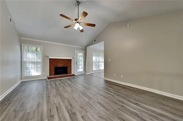 an empty room with wooden floor fireplace and windows