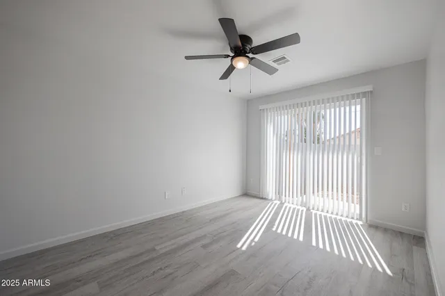 an empty room with wooden floor fan and windows