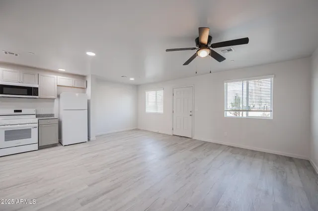 an empty room with wooden floor a ceiling fan and windows