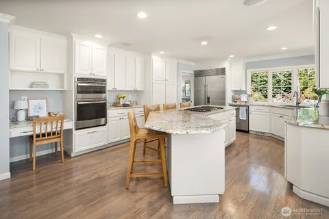 a kitchen with stainless steel appliances granite countertop a stove top oven a sink dishwasher and a refrigerator with wooden floor