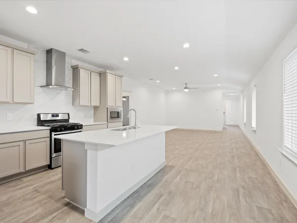 a large white kitchen with stainless steel appliances granite countertop a stove a sink a refrigerator and white cabinets with wooden floor