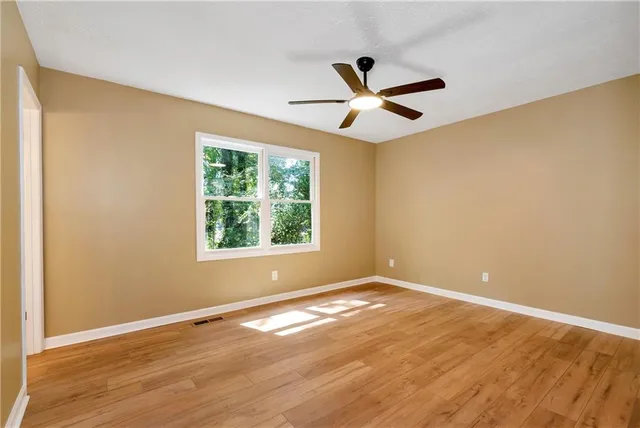 a view of empty room with wooden floor and fan