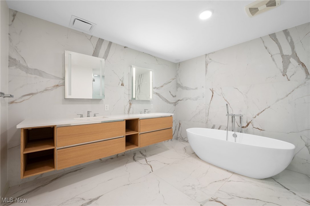 22700 Lake Road, Unit 204 Rocky River, OH 44116 - Photo 16 of 31 Bathroom featuring stone wall, double vanity, a freestanding bath, and recessed lighting