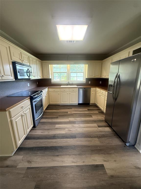 304 6th Street Northwest Springhill, LA 71075 - Photo 19 of 38 Kitchen featuring wood-finish flooring, cream-colored cabinetry, built-in stainless steel appliances, and a double window