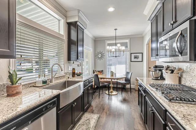 a kitchen with stainless steel appliances granite countertop a sink a stove top oven a refrigerator with wooden cabinets and floor