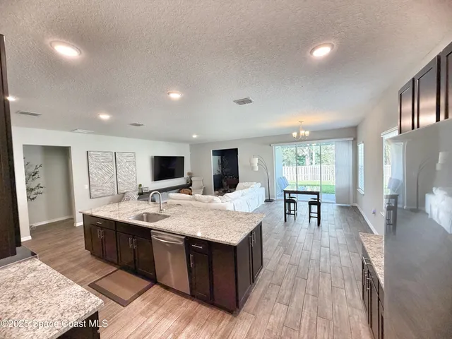 a living room with stainless steel appliances granite countertop furniture wooden floor and a kitchen view