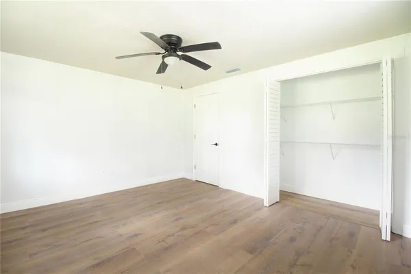 an empty room with wooden floor chandelier fan and windows