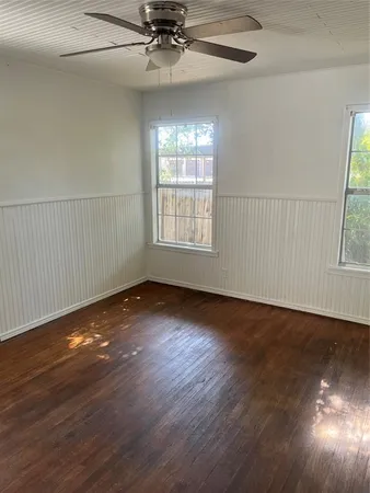 an empty room with wooden floor fan and windows