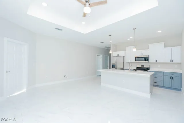 a large white kitchen with kitchen island a sink a stove a refrigerator and a dining table with wooden floor