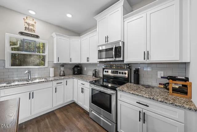 a kitchen with granite countertop stainless steel appliances white cabinets and a window