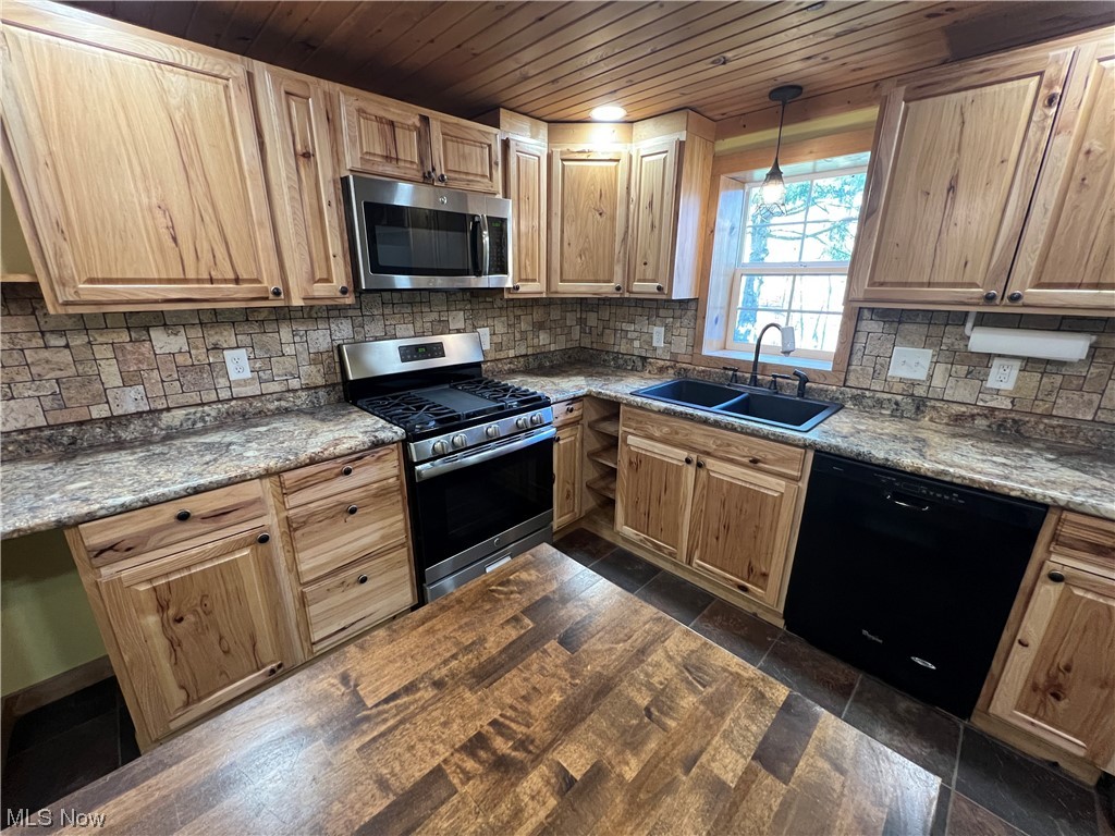 Kitchen featuring tasteful backsplash, dark stone countertops, stainless steel appliances, sink, and hanging light fixtures