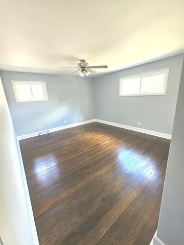 an empty room with wooden floor fan and windows