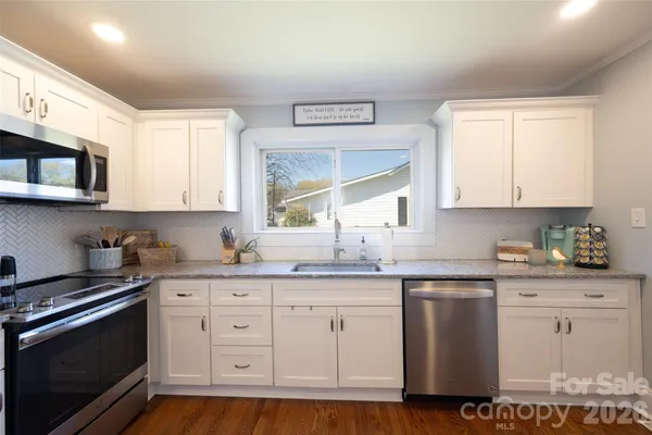 a kitchen with granite countertop white cabinets stainless steel appliances and a window