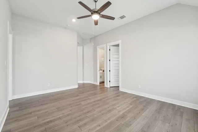 an empty room with wooden floor ceiling fan and windows