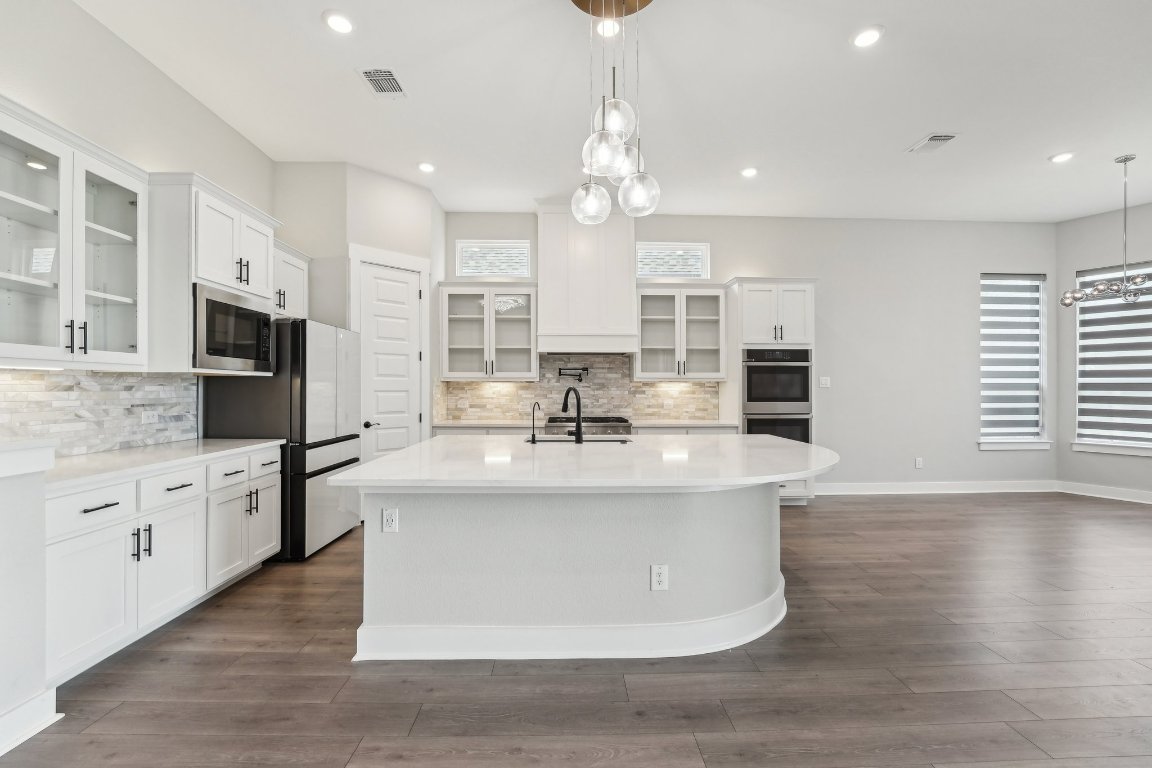 4216 Caroline Mae Cove Pflugerville, TX 78660 - Photo 8 of 32 a kitchen with stainless steel appliances granite countertop a sink a stove a refrigerator and island with wooden floor