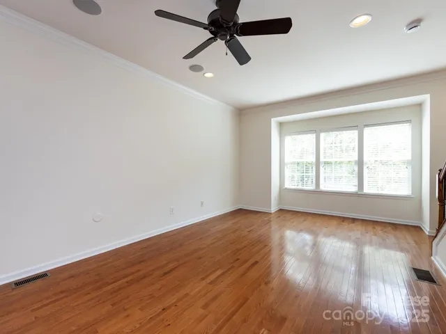 an empty room with wooden floor fan and windows
