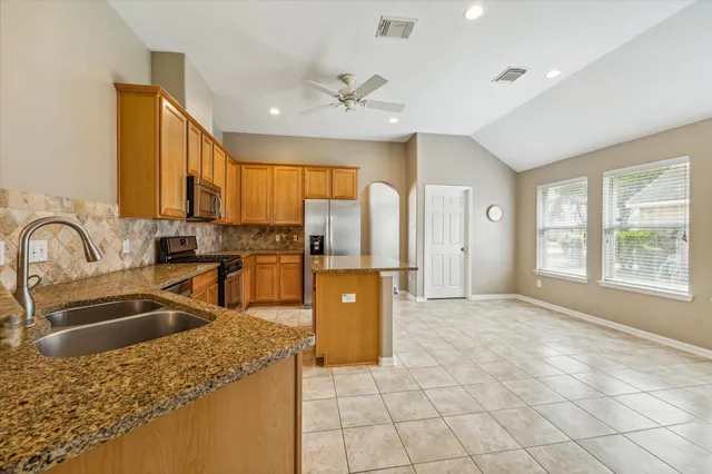 a kitchen with stainless steel appliances granite countertop a refrigerator a sink a stove top oven and a dining table