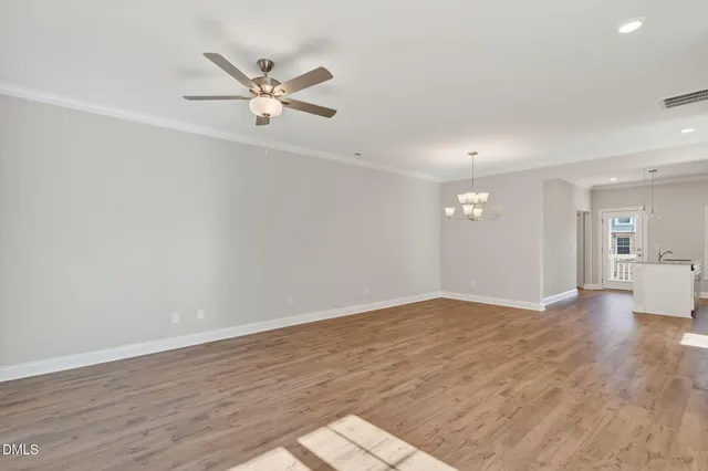 a view of an empty room with wooden floor and a ceiling fan