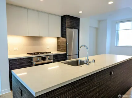 a view of an empty room with wooden floor and a kitchen