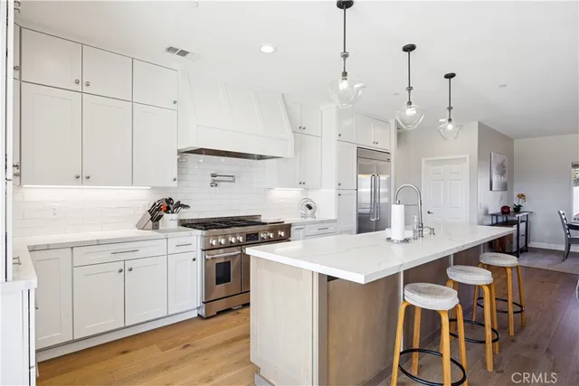 a open kitchen with stainless steel appliances granite countertop a stove a sink a kitchen island with white cabinets and wooden floor