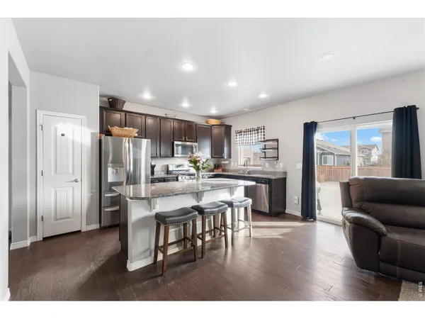 a living room with stainless steel appliances kitchen island granite countertop furniture and a wooden floor