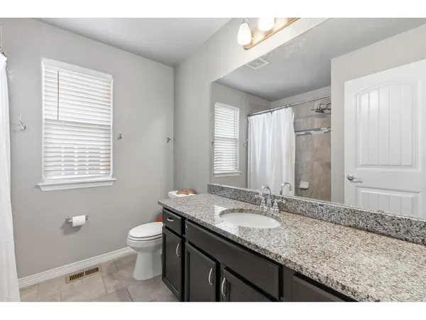 a bathroom with a granite countertop sink a toilet a mirror and a window