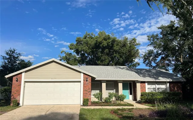 a view of a house with a yard plants and large tree