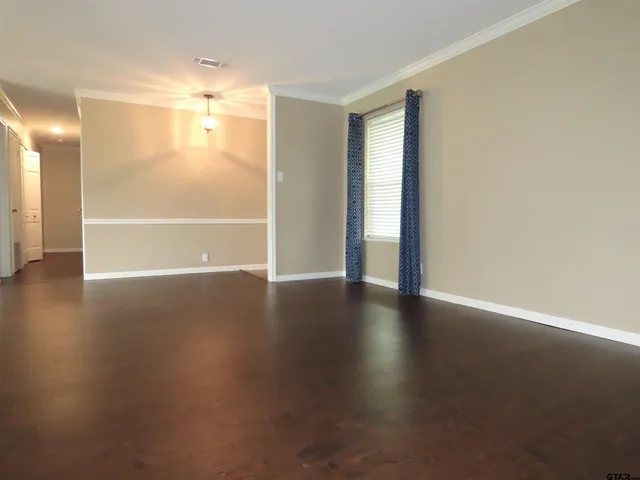 an empty room with wooden floor and windows with curtains