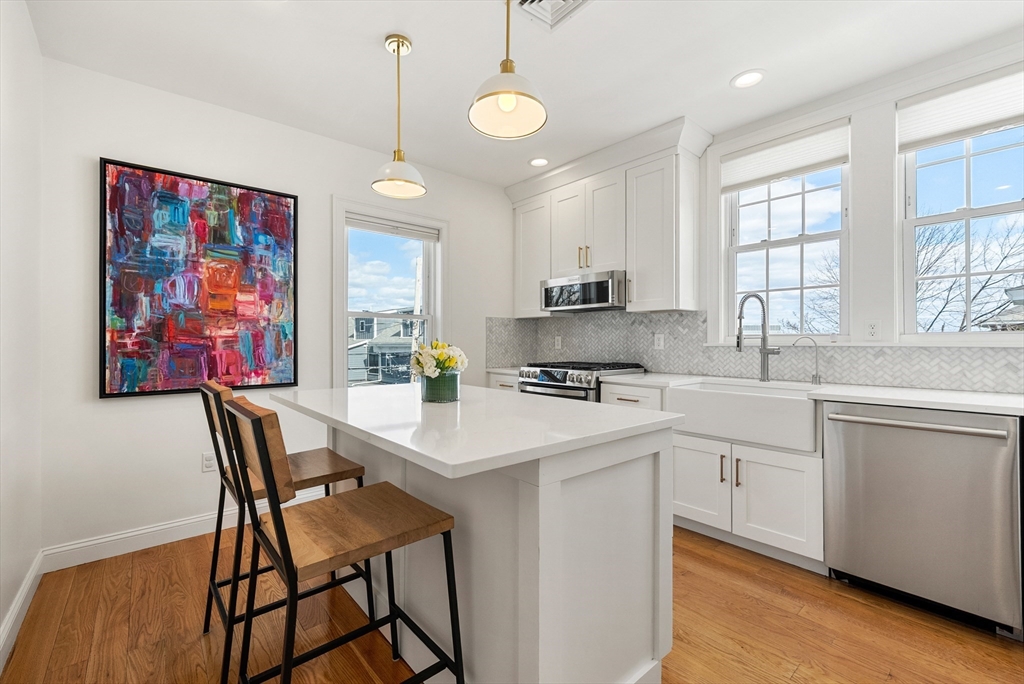 25 Fenwick Street, Unit 2 Somerville, MA 02145 - Photo 3 of 22 a white kitchen with stainless steel appliances granite countertop a sink a stove a dining table and chairs