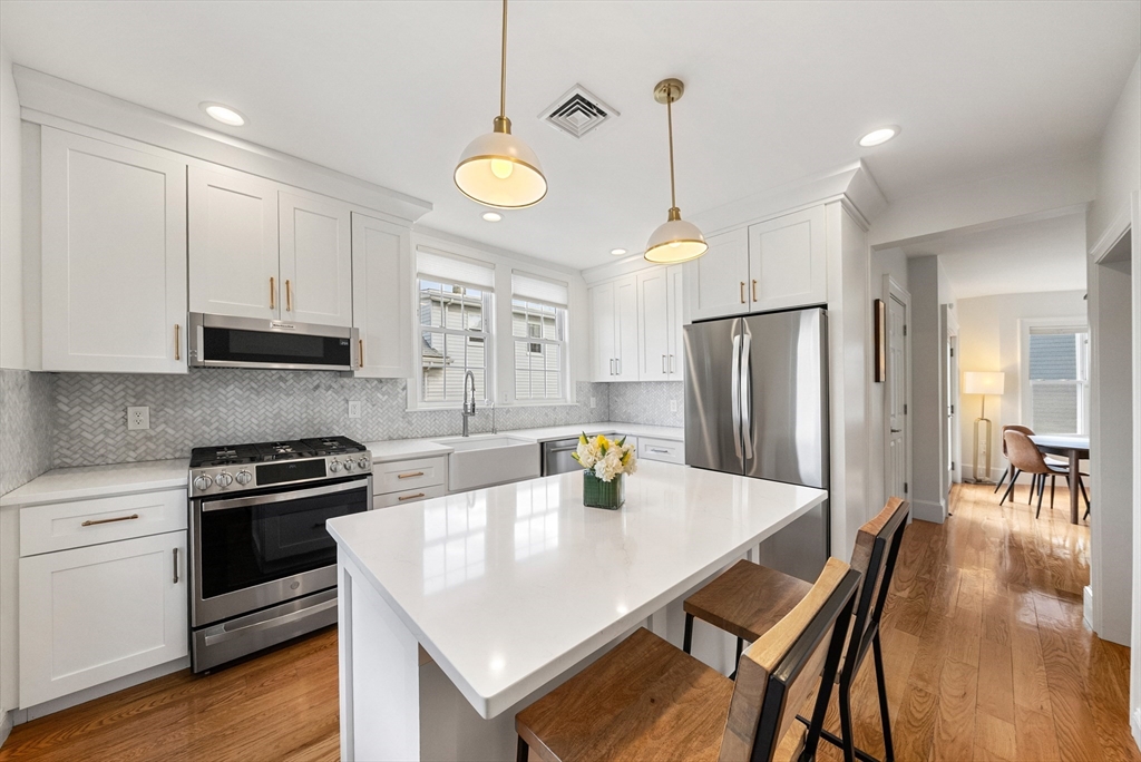 25 Fenwick Street, Unit 2 Somerville, MA 02145 - Photo 4 of 22 a kitchen with stainless steel appliances granite countertop a stove a refrigerator a microwave a dining table and chairs with wooden floor