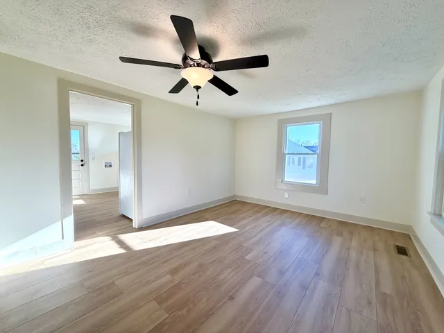 an empty room with wooden floor fan and windows