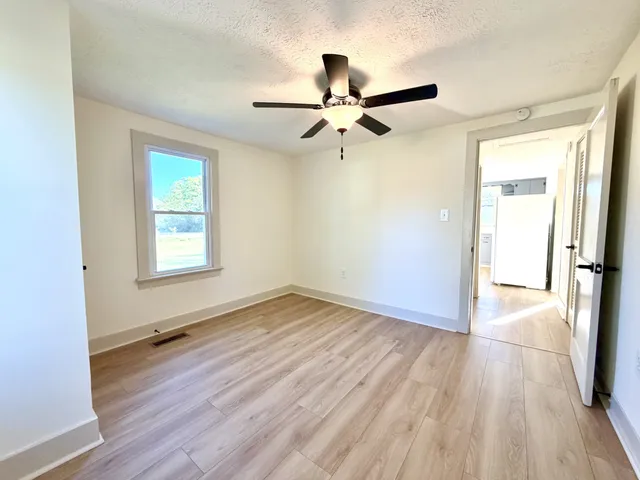 an empty room with wooden floor a ceiling fan and windows