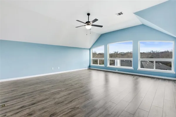 a view of an empty room with wooden floor and a ceiling fan