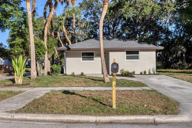 a view of a white house next to a yard with big trees