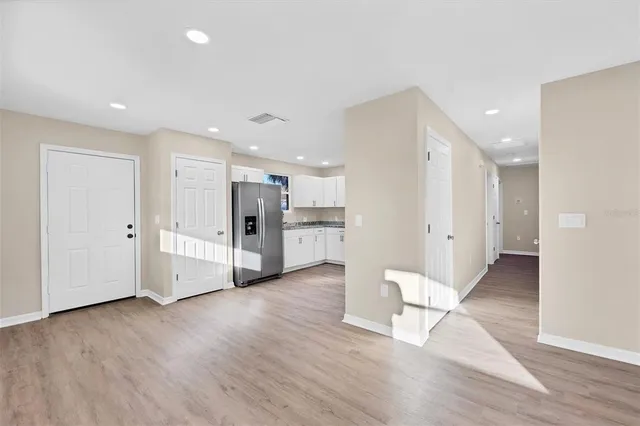 a view of an empty room with wooden floor and a kitchen