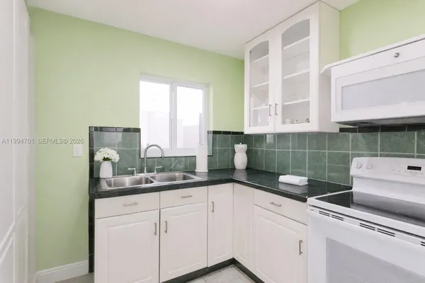 a kitchen with stainless steel appliances granite countertop a sink dishwasher and a black refrigerator with white cabinets