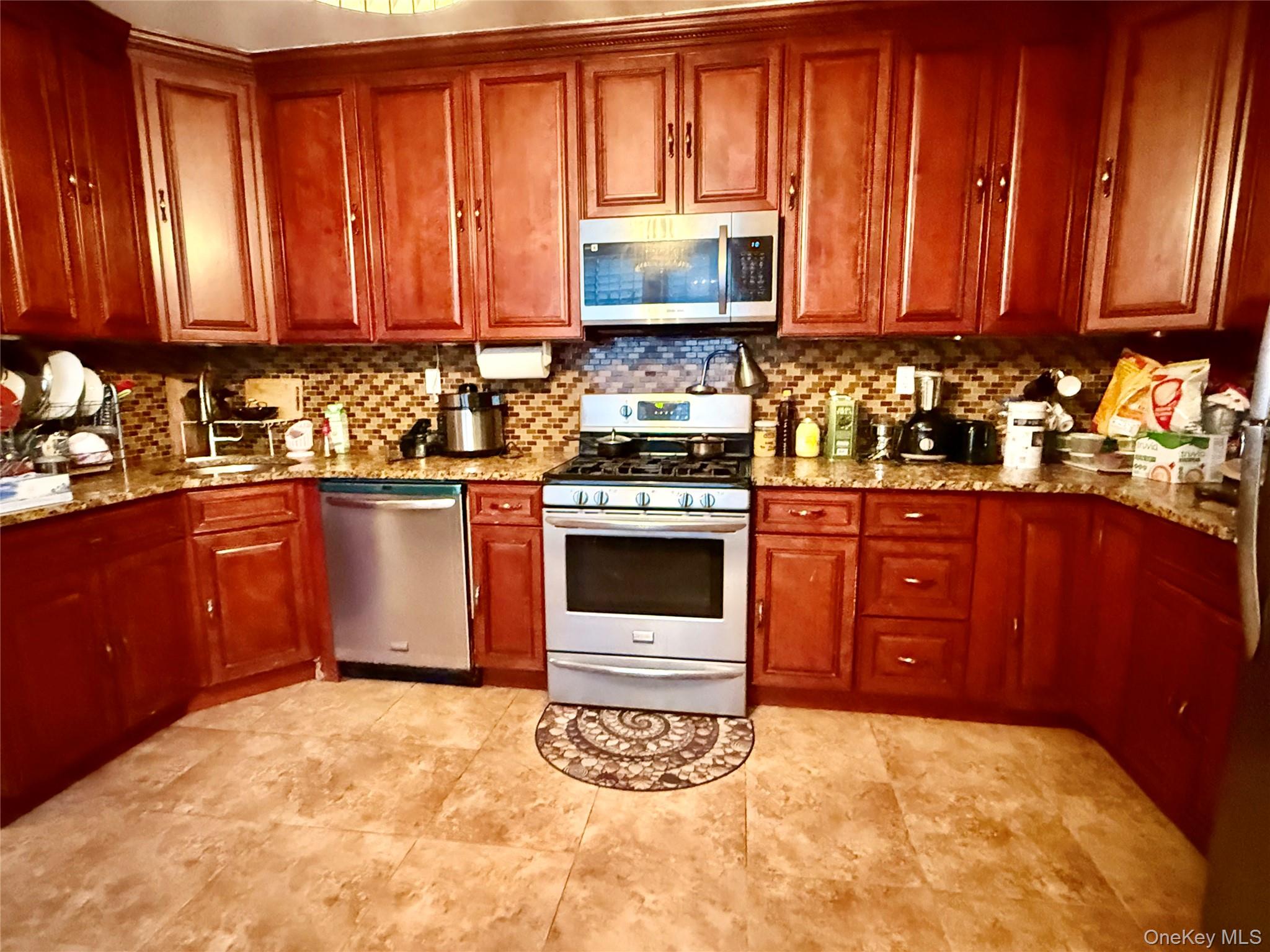 54-05 68th Street Queens, NY 11378 - Photo 11 of 47 Kitchen with stainless steel appliances, light stone counters, and brown cabinets