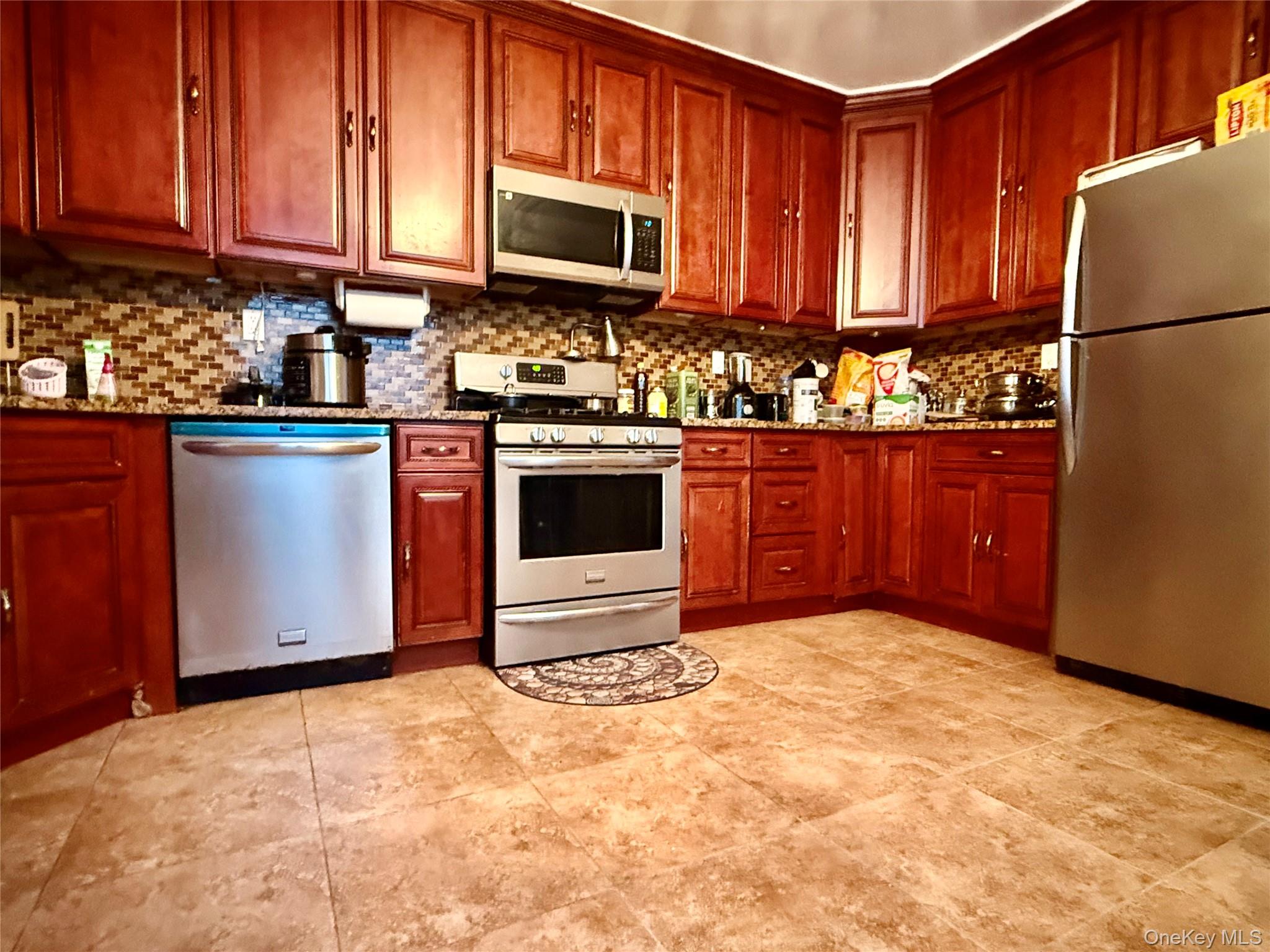54-05 68th Street Queens, NY 11378 - Photo 12 of 47 Kitchen with stainless steel appliances, dark stone counters, decorative backsplash, and dark brown cabinets
