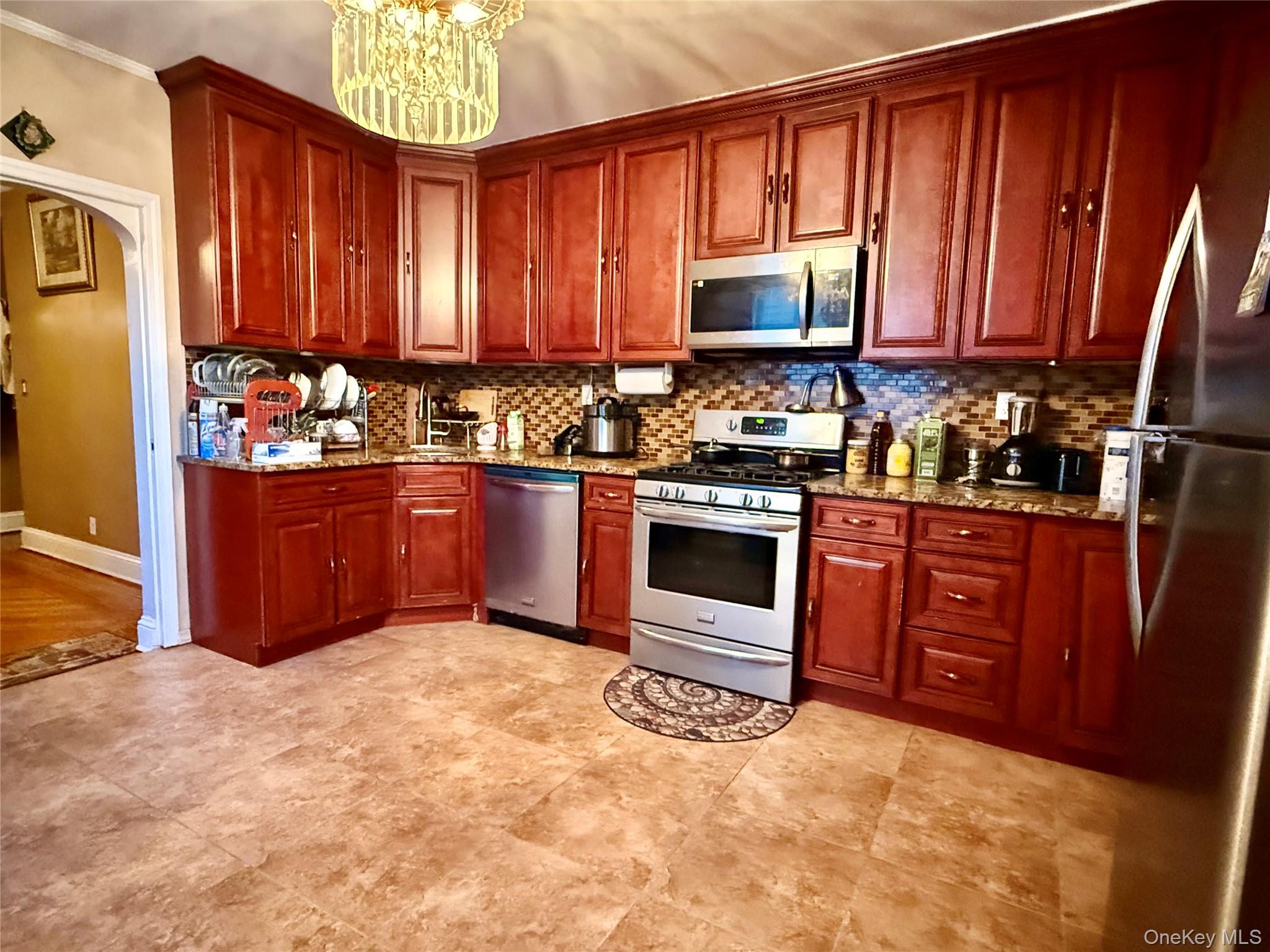 54-05 68th Street Queens, NY 11378 - Photo 13 of 47 Kitchen featuring stainless steel appliances, light stone countertops, arched walkways, tasteful backsplash, and a chandelier