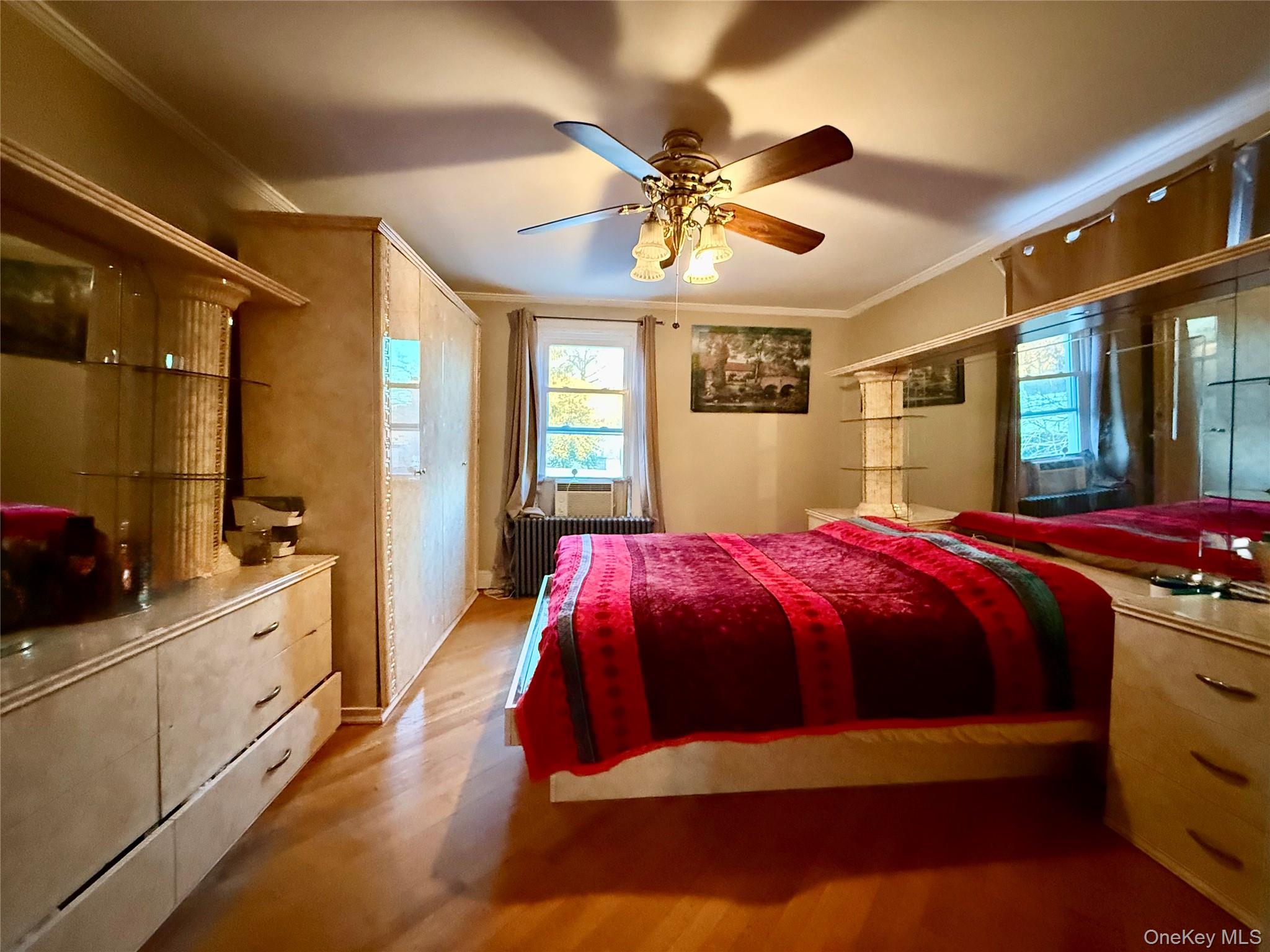 54-05 68th Street Queens, NY 11378 - Photo 20 of 47 Third bedroom featuring crown molding, radiator heating unit, light wood-style floors, ceiling fan, and multiple windows