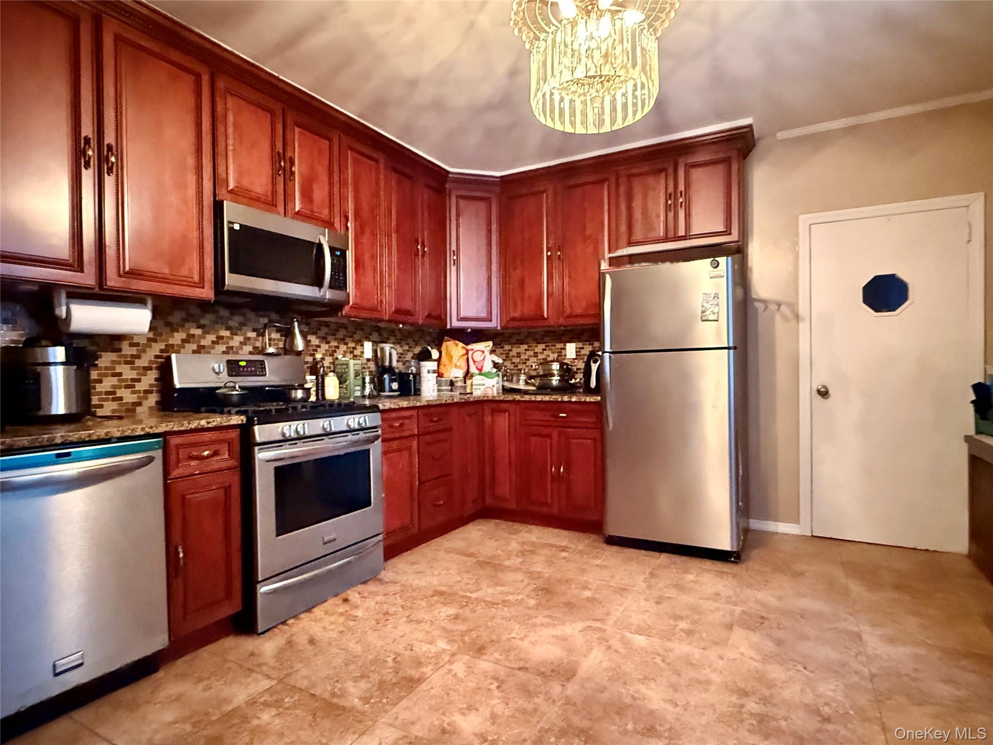 54-05 68th Street Queens, NY 11378 - Photo 9 of 47 Kitchen featuring stainless steel appliances, light stone countertops, a chandelier, tasteful backsplash, and dark brown cabinets