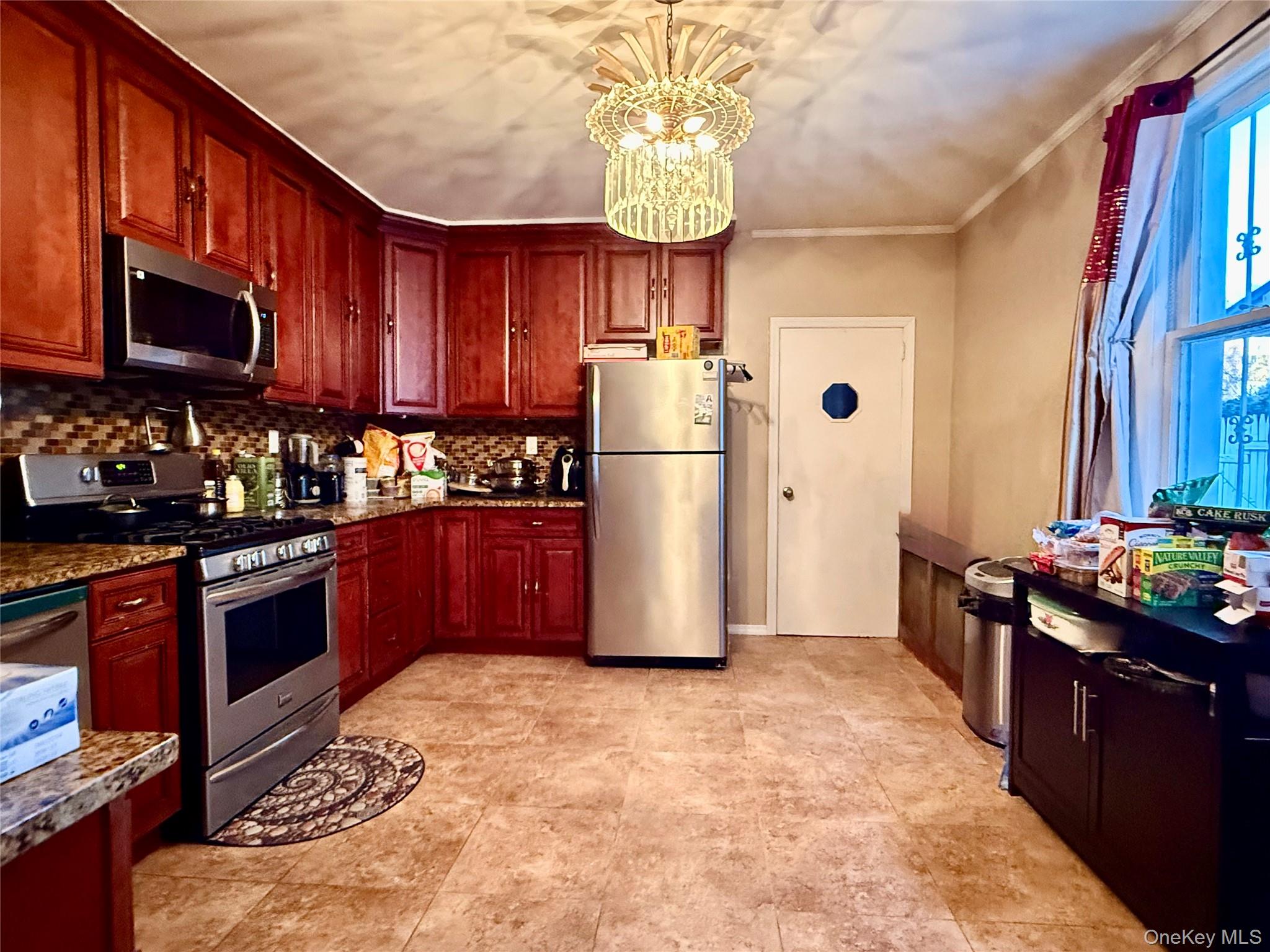 54-05 68th Street Queens, NY 11378 - Photo 10 of 47 Kitchen with appliances with stainless steel finishes, dark brown cabinets, decorative backsplash, ornamental molding, and a chandelier