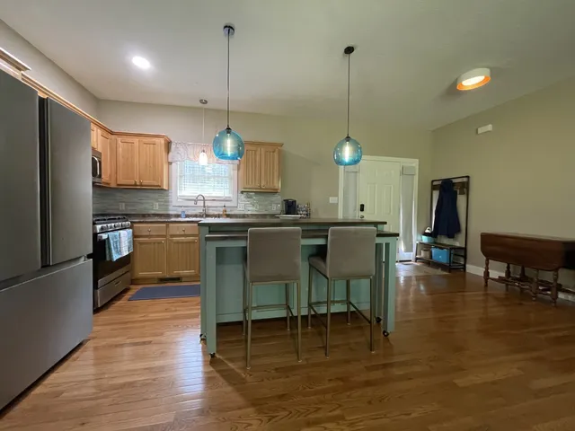a kitchen with stainless steel appliances granite countertop a stove a refrigerator a kitchen island a dining table and chairs with wooden floor