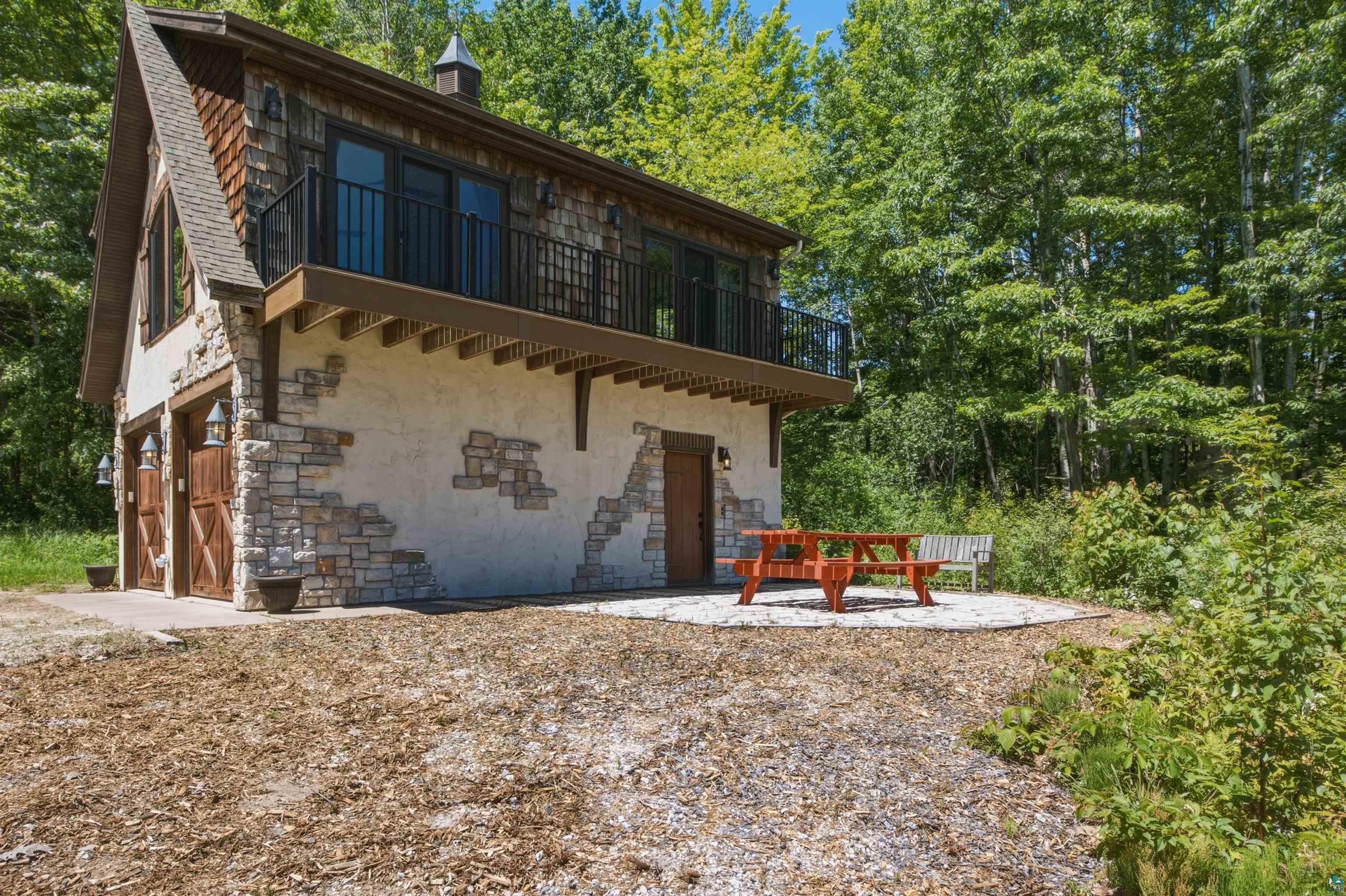 86270 Meyers-Olson Road Bayfield, WI 54814 - Photo 26 of 33 Stone and stucco exterior featuring wood-paneled garage doors, a second-story balcony with iron railing, and a gabled roofline with cedar shake siding